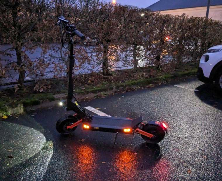 Electric scooter parked at dusk with its deck lights on